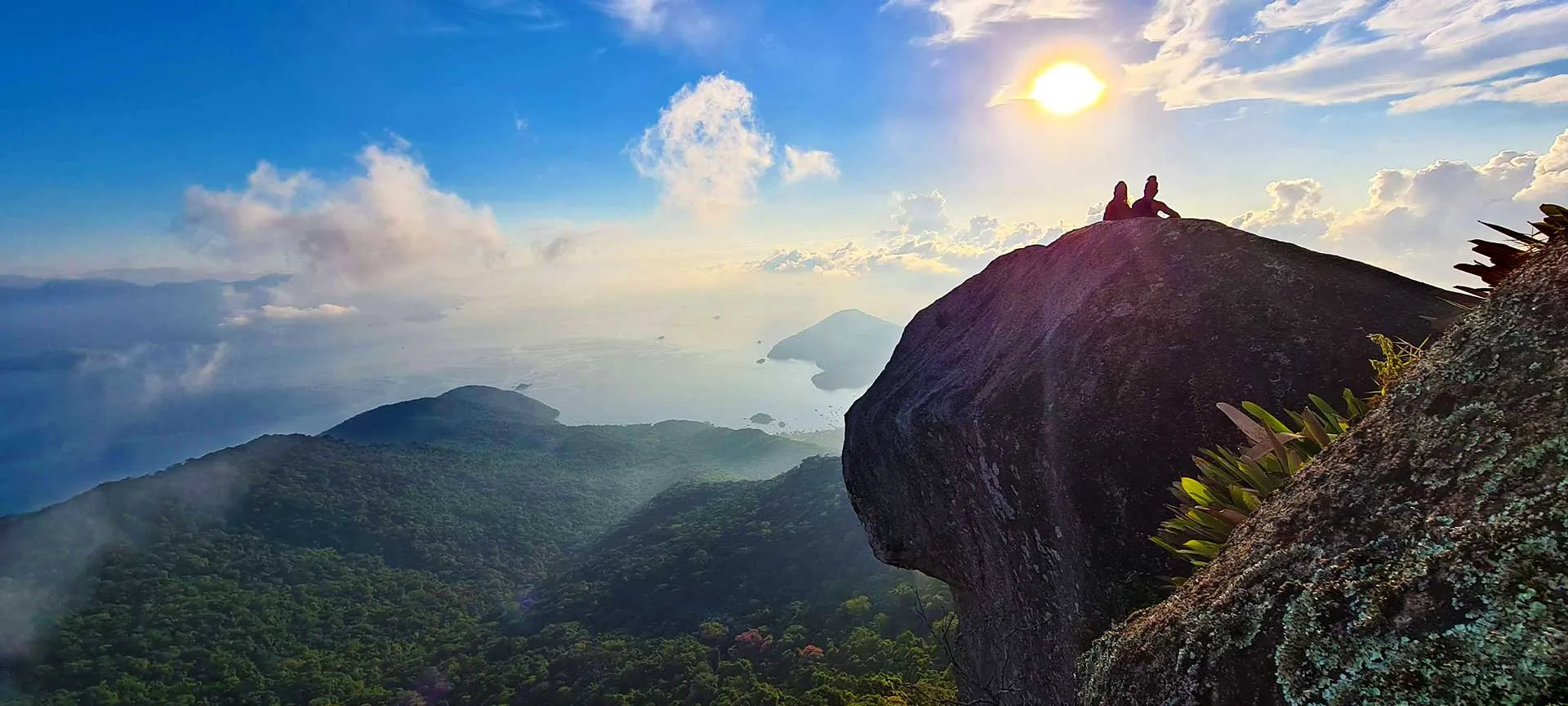 Hikers on the Pico do Papagaio summit at sunrise above the bay, Ilha Grande